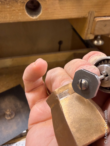 I'm holding a flex shaft just outside of the frame. The end of the shaft has an uneven octagon on the end. The vase is held next to the tool. Some planishing marks appear on the neck of the vase